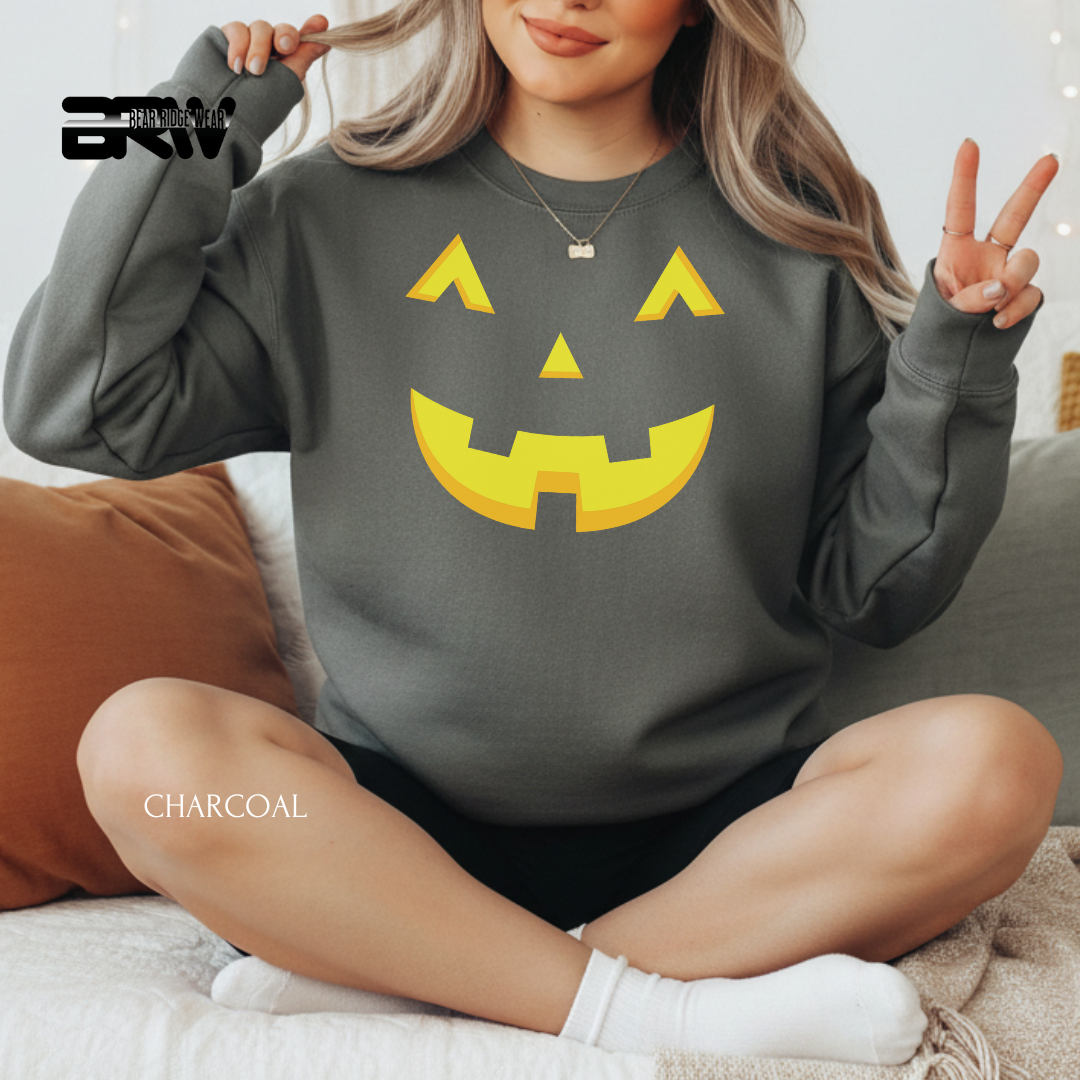 Person wearing a charcoal gray sweatshirt with a yellow jack-o'-lantern face design, sitting on a couch.