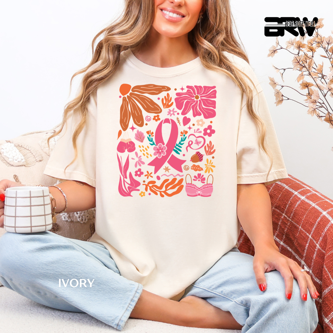 Woman wearing a white t-shirt with pink and orange floral and ribbon design, sitting on a couch. BREAST CANCER AWARENESS TEE
