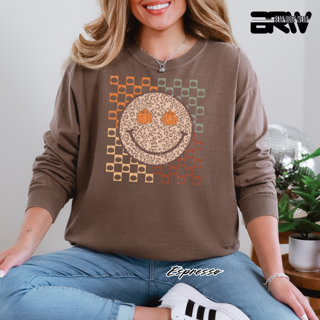 Woman wearing a brown sweatshirt with a smiley face design, sitting indoors.