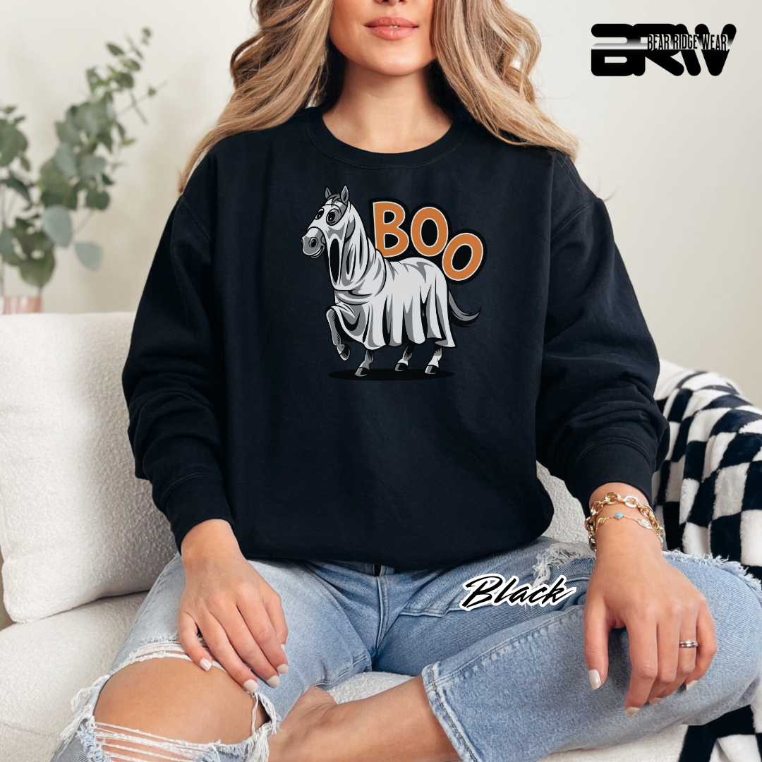Person wearing a black sweatshirt with a ghost horse graphic and 'BOO' text, sitting on a couch.
