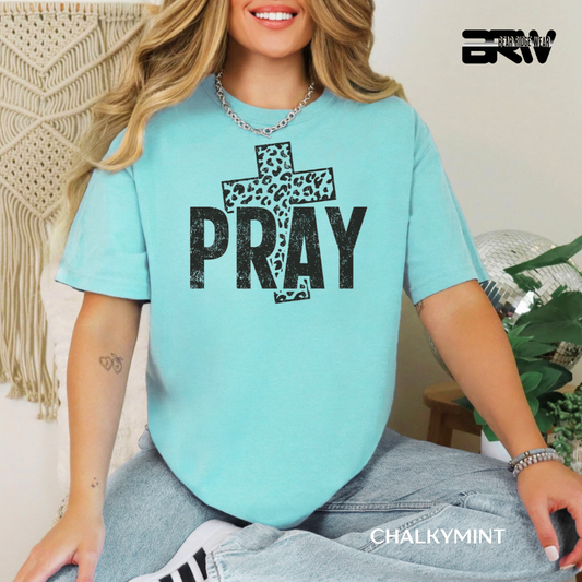 Person wearing a light blue t-shirt with a cross and 'PRAY' text, sitting in a casual setting.
