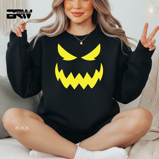 Person wearing a black sweatshirt with a yellow angry face design, sitting on a couch.