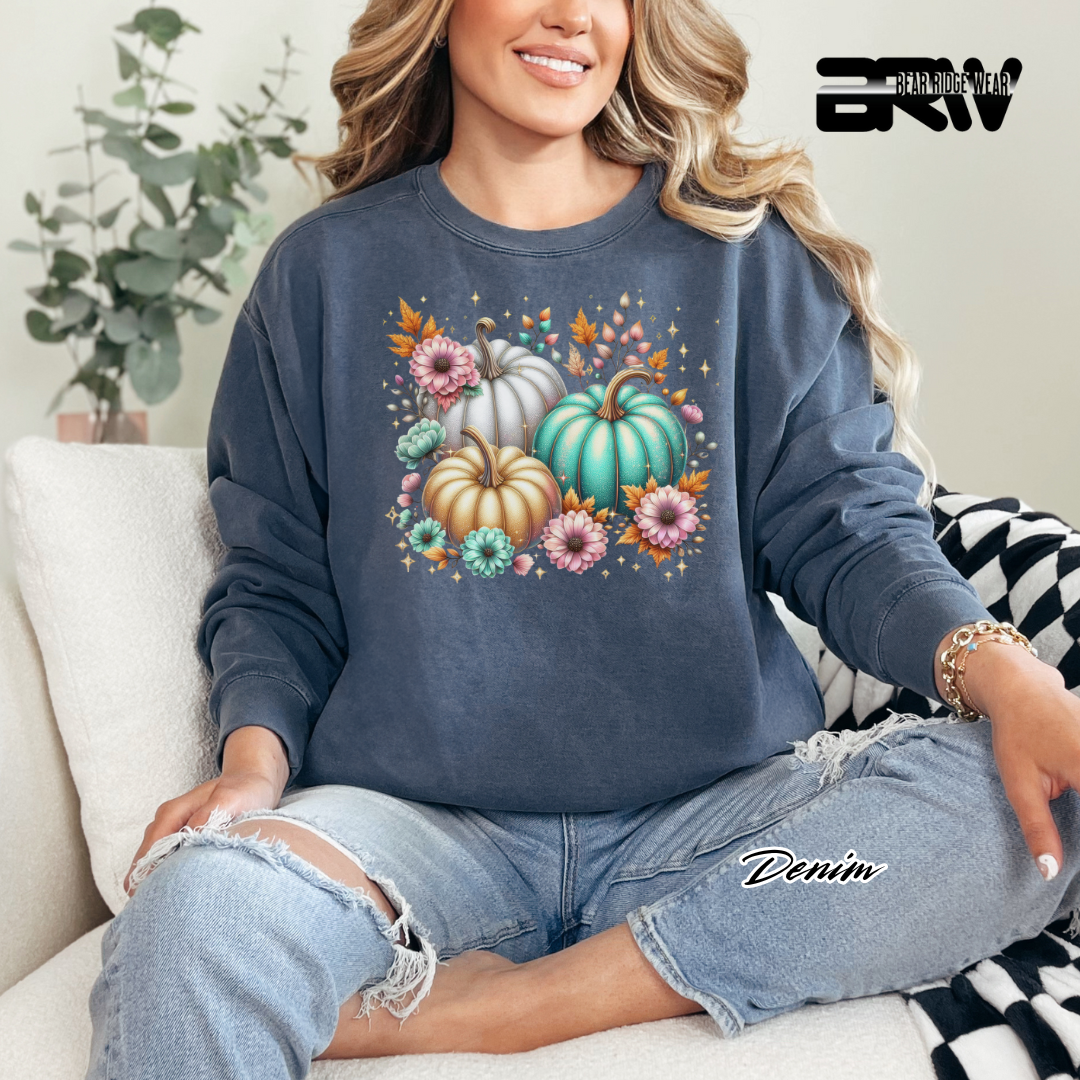 Woman wearing a blue sweatshirt with pumpkins and flowers sitting on a couch.
