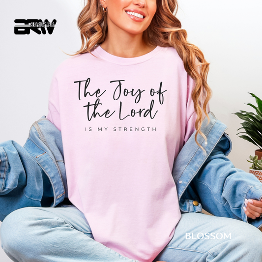 Person wearing a pink sweatshirt with 'The Joy of the Lord is my strength' text, sitting on a couch.