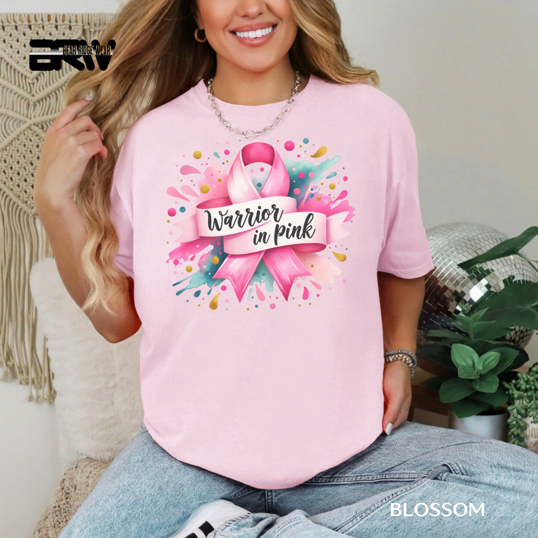 Woman wearing a pink t-shirt with a breast cancer awareness design, sitting on a couch.