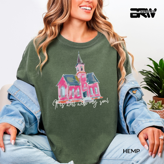 Person wearing a green sweatshirt with a pink house design and text, sitting on a couch.