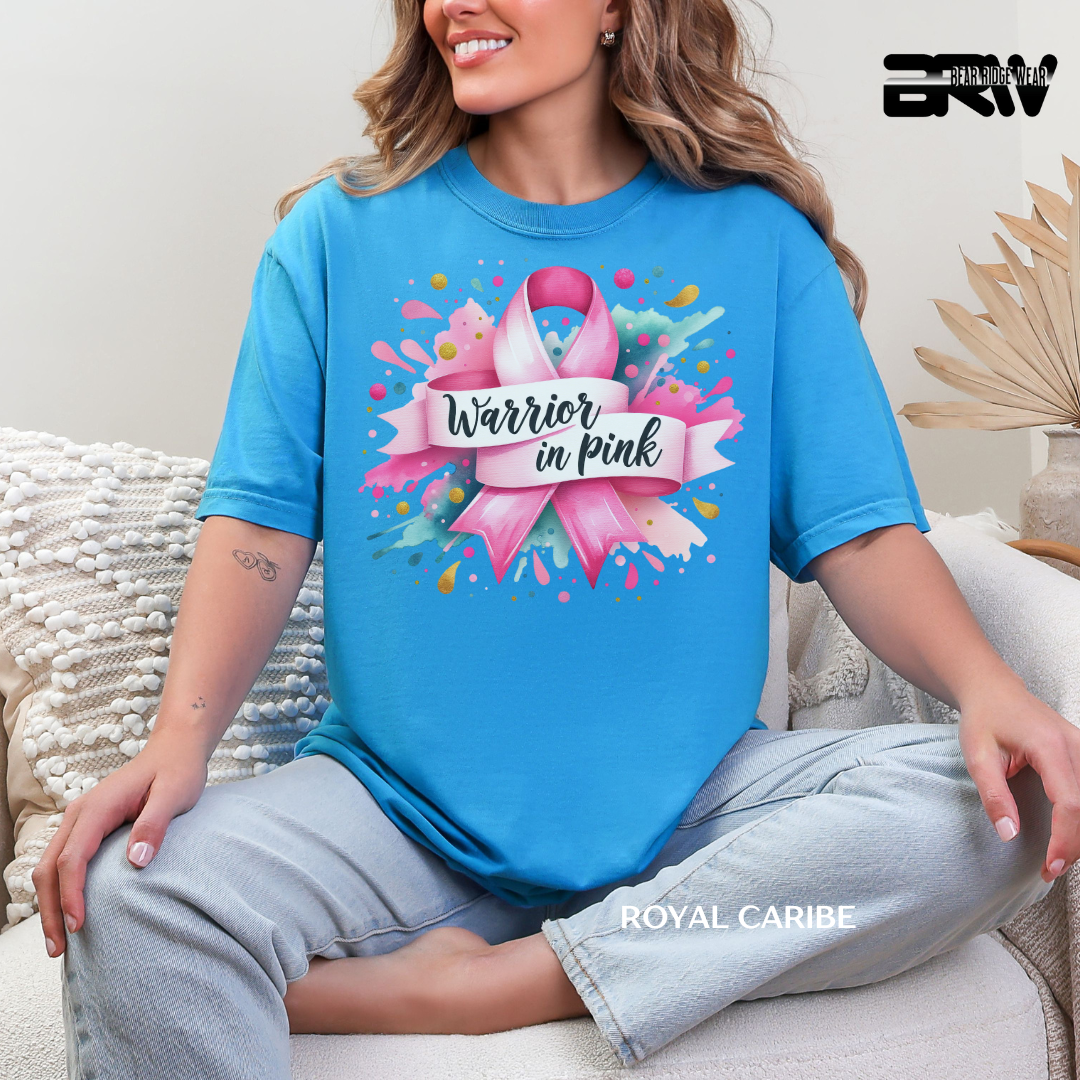 Woman wearing a blue t-shirt with a pink ribbon design and 'Warrior in Pink' text, sitting on a couch.