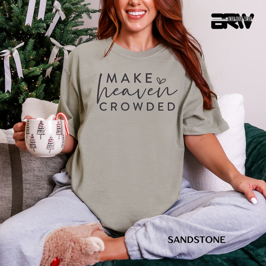 Woman wearing a 'Make Heaven Crowded' shirt, holding a mug, with a Christmas tree in the background.