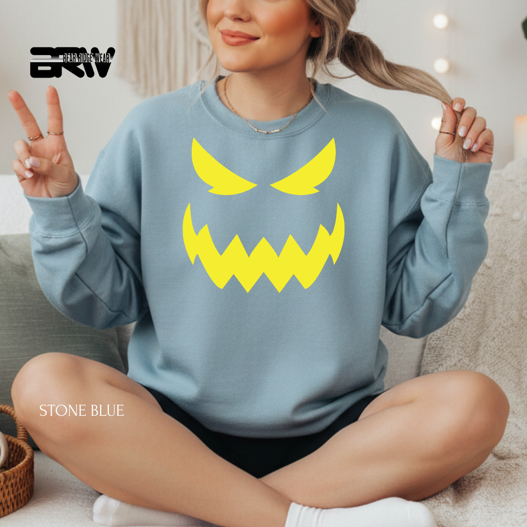 Person wearing a stone blue sweatshirt with a yellow angry face design, sitting on a couch.