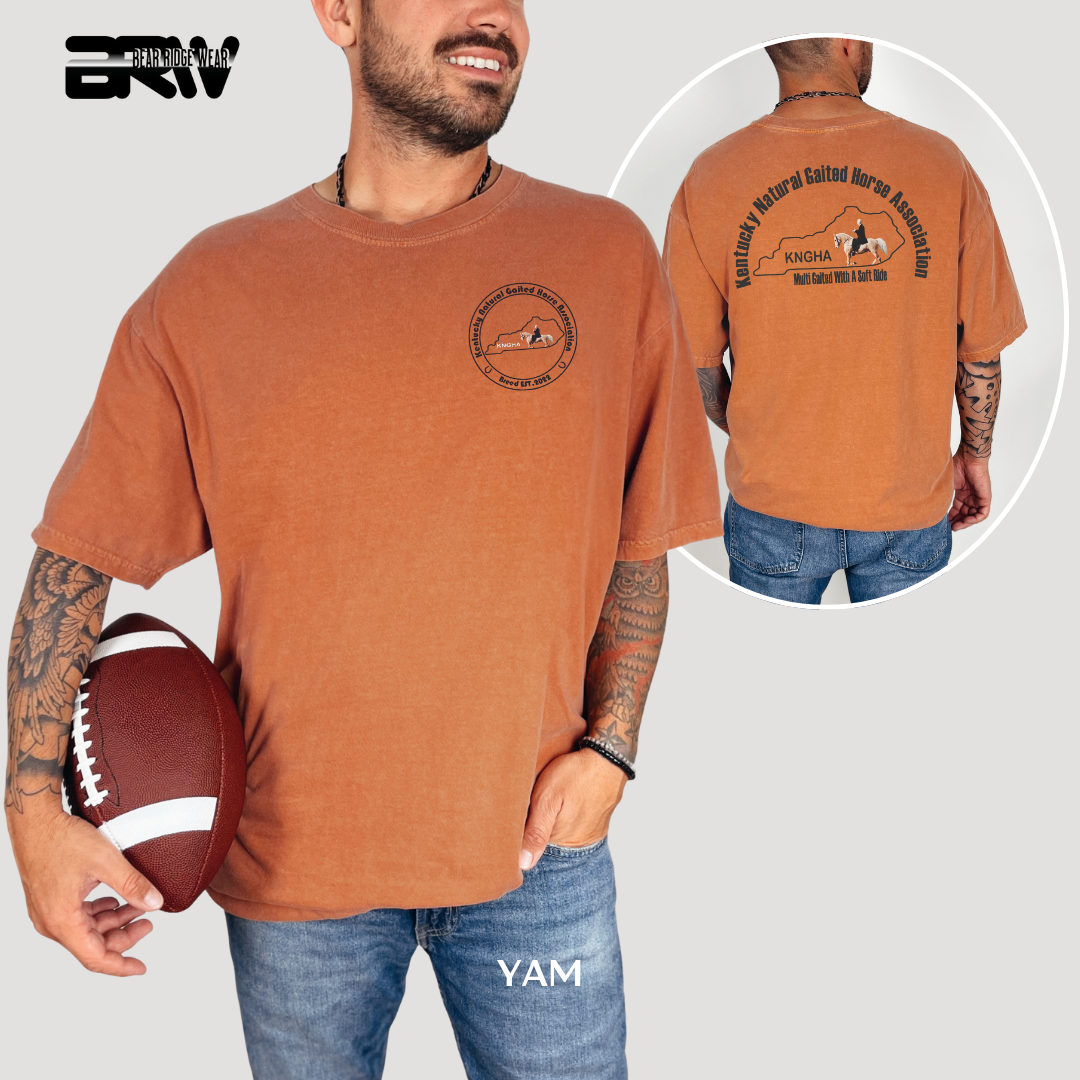 Man wearing a brown t-shirt with graphics and text, holding a football, on a plain background.