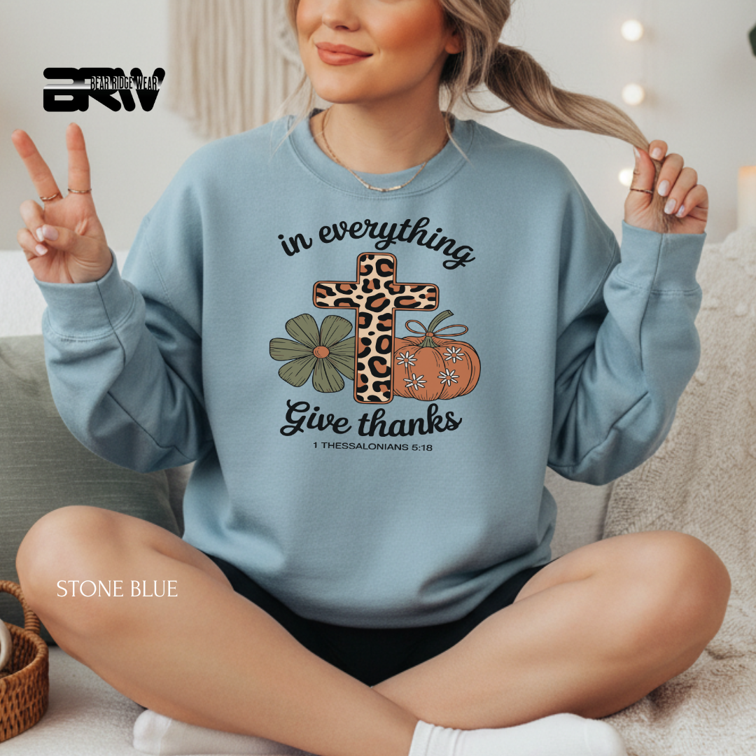 Person wearing a stone blue sweatshirt with a cross, pumpkin, and flowers design, sitting on a couch.
