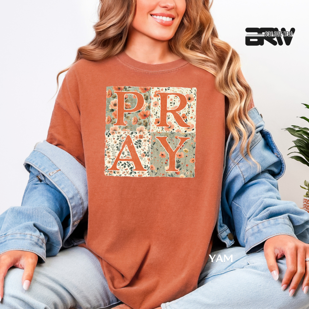 Person wearing a brown sweatshirt with 'PRAY' print, sitting against a light background.