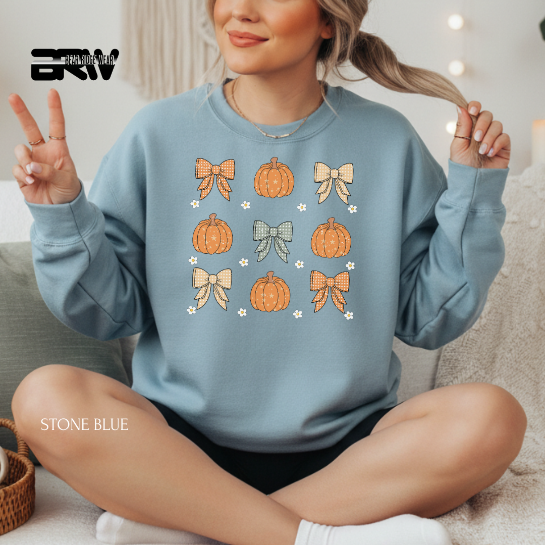 Woman wearing a stone blue sweatshirt with pumpkins and bows design, sitting on a couch.