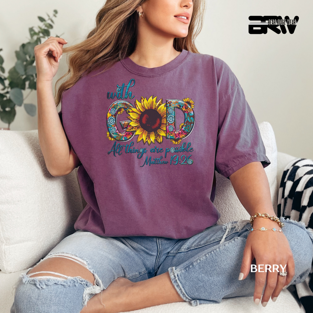 Person wearing a purple t-shirt with a colorful design and text, sitting on a couch. WITH GOD ALL THINGS ARE POSSIBLE FAITH TEE