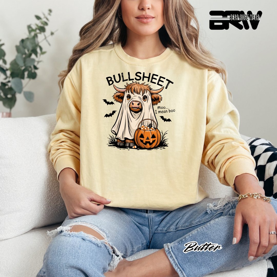 Person wearing a yellow sweatshirt with a Halloween-themed design, sitting on a couch.