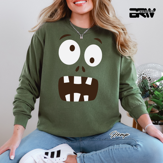 Person wearing a green sweatshirt with a cartoon face design, sitting indoors.