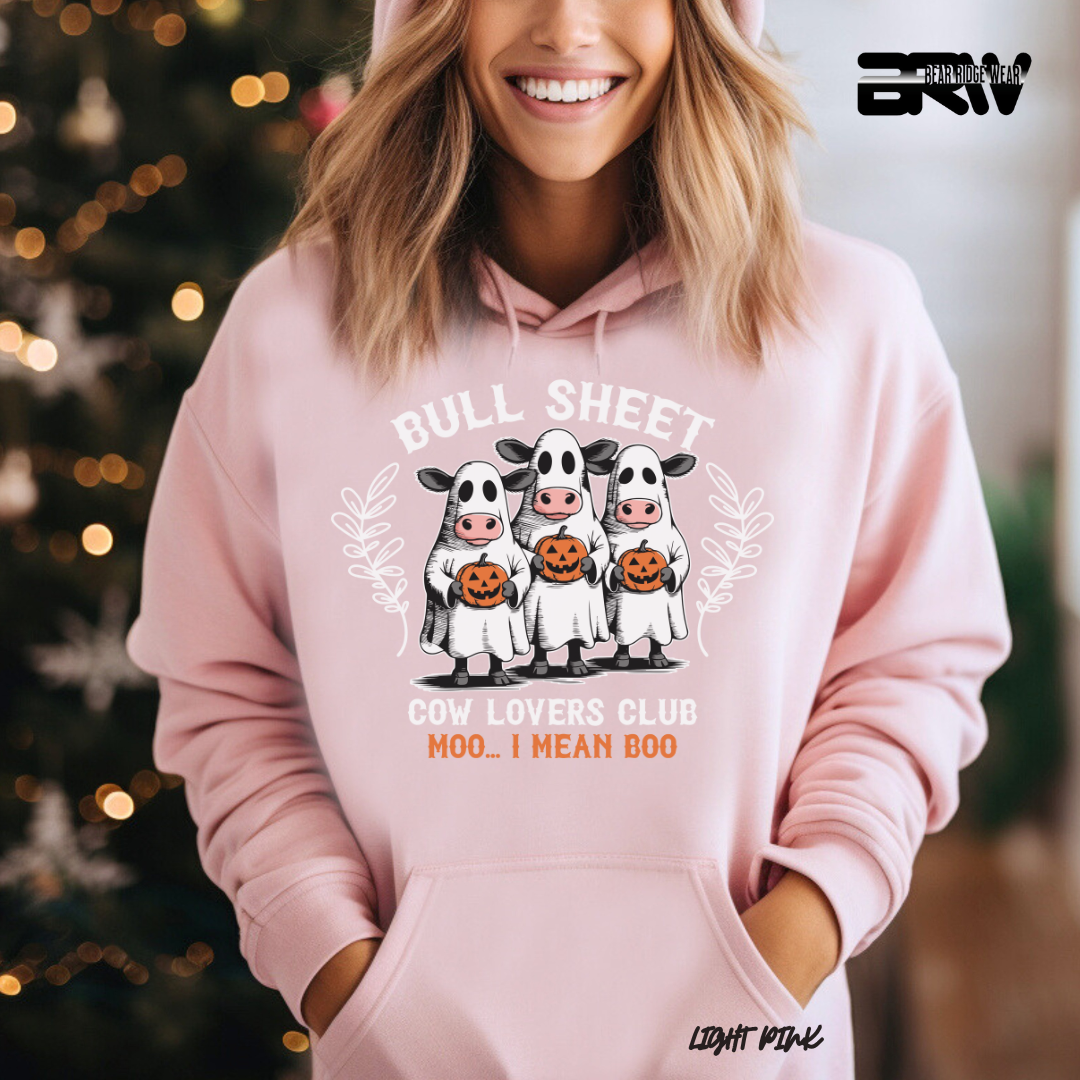 Person wearing a pink hoodie with cow-themed design and text, standing in front of a decorated Christmas tree.