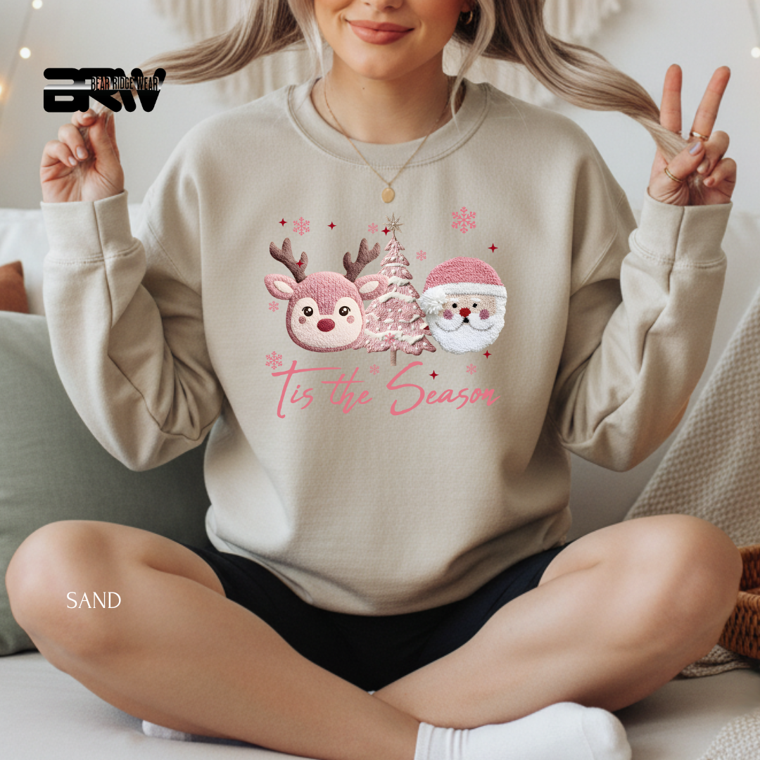 Person wearing a beige sweatshirt with Christmas design and text, sitting on a couch.