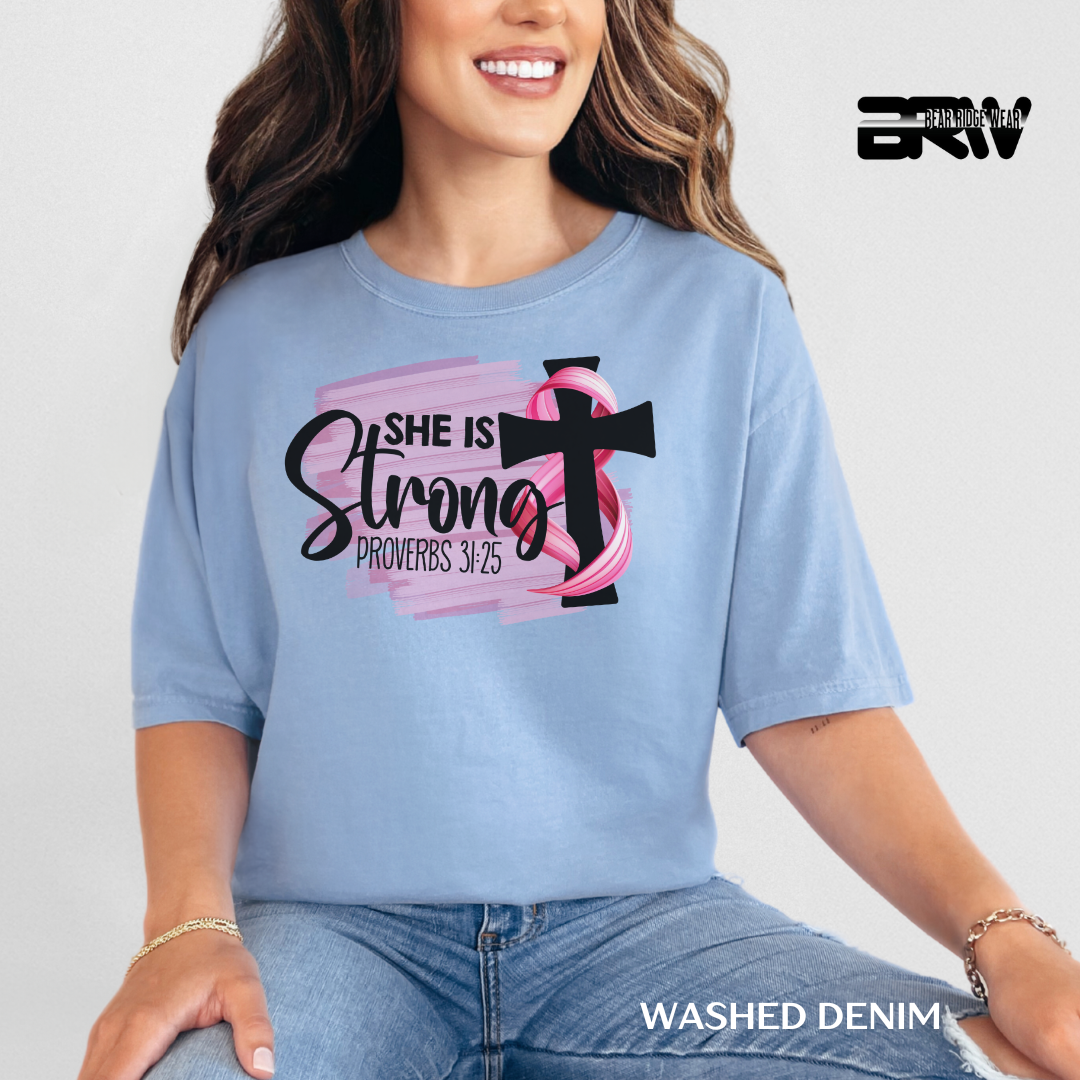 Woman wearing a blue t-shirt with a pink ribbon and cross design, sitting against a light gray background.