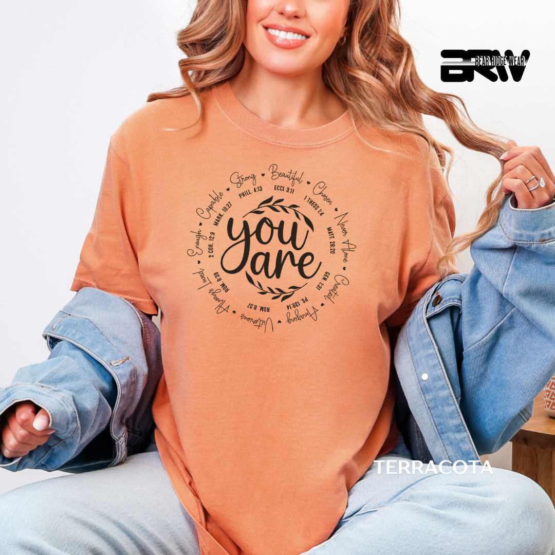 Woman wearing a terracotta-colored t-shirt with text design, sitting on a white background.