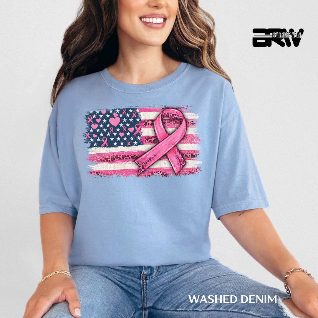 Woman wearing a blue t-shirt with a pink ribbon and American flag design, sitting on a white background.