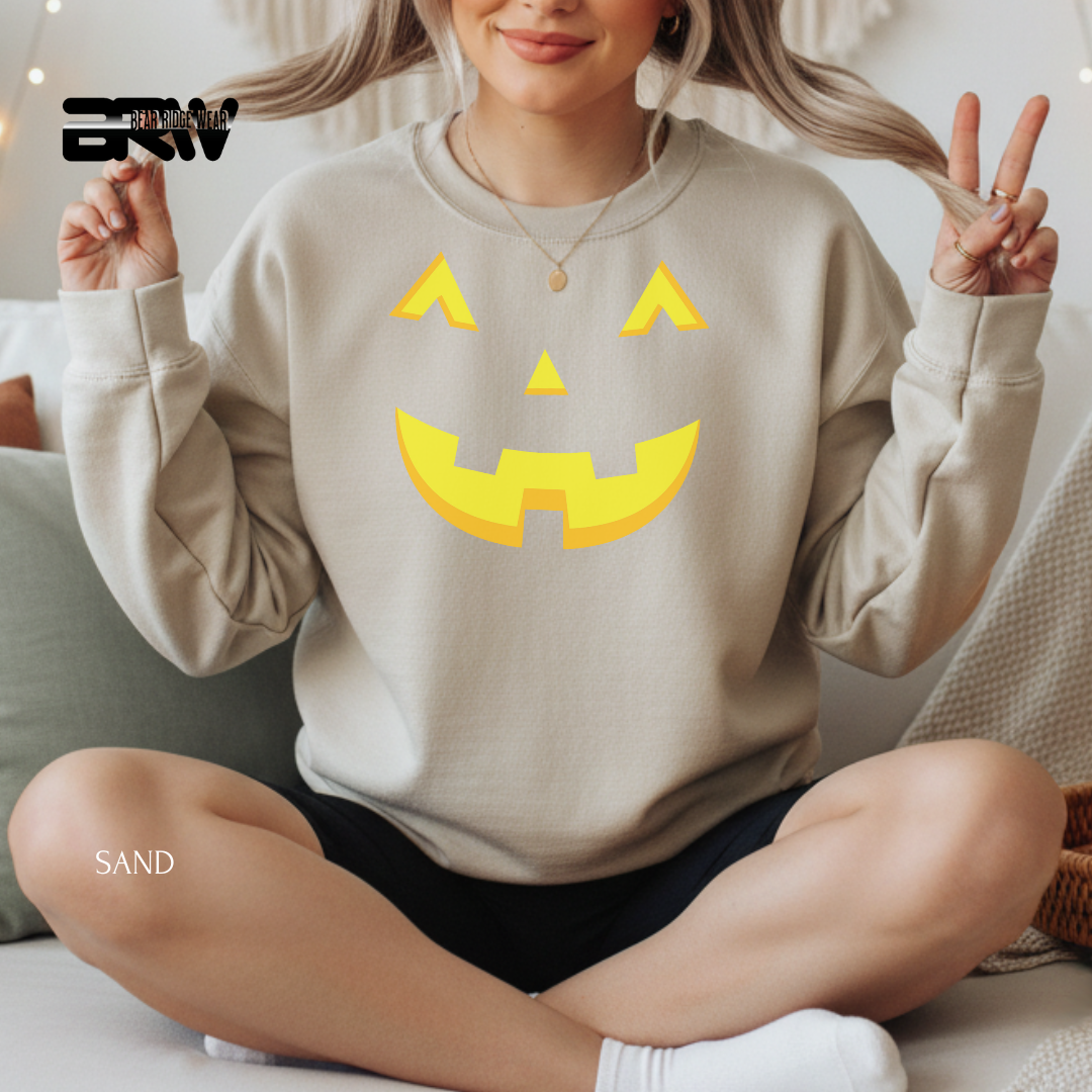 Person wearing a beige sweatshirt with a yellow jack-o'-lantern face design, sitting on a couch.
