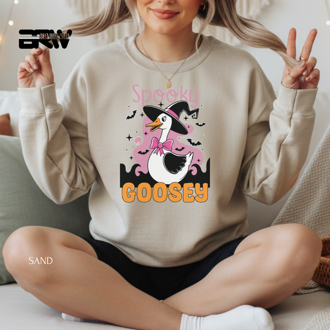 Person wearing a beige sweatshirt with a cartoon goose design and text, sitting on a couch.