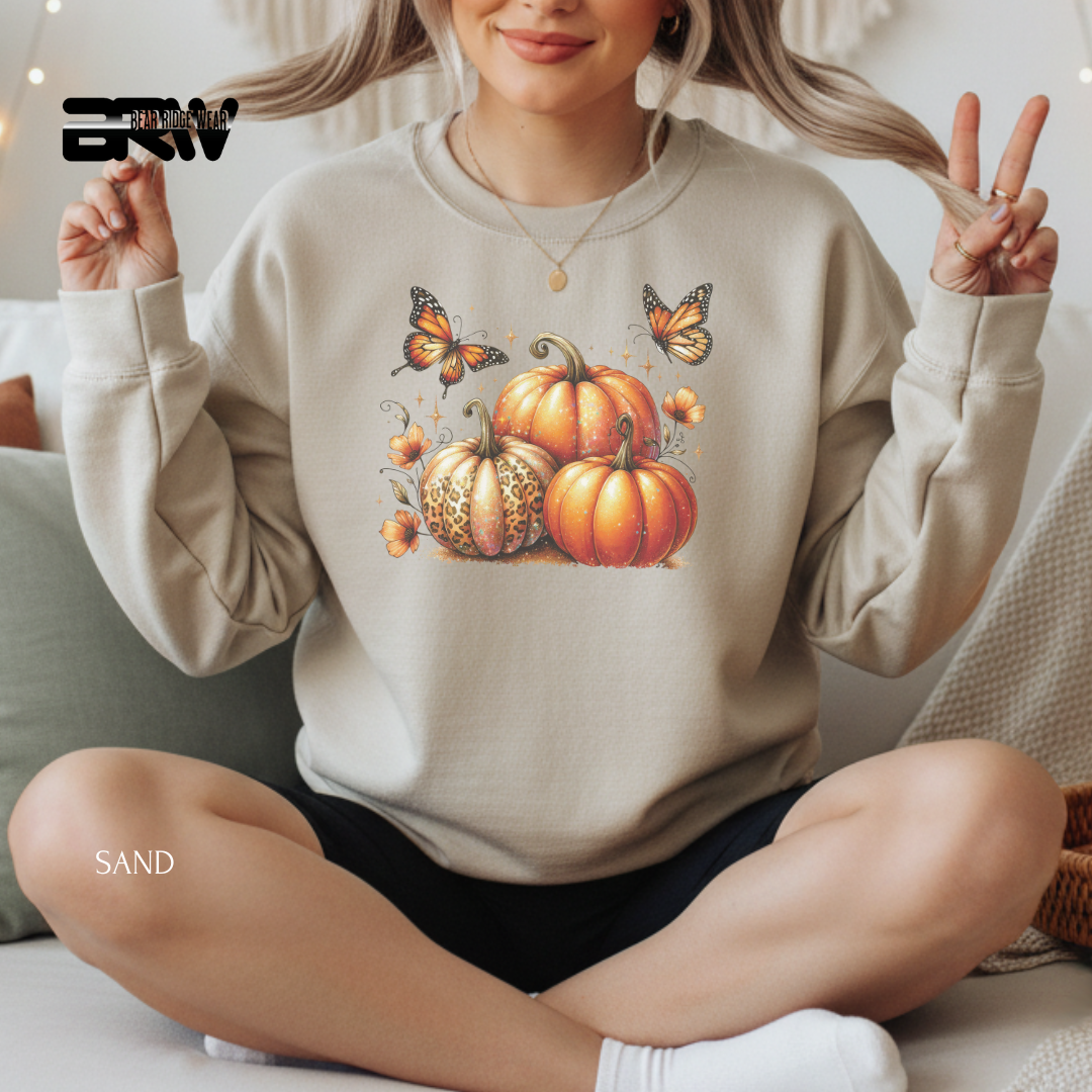 Person wearing a beige sweatshirt with pumpkin and butterfly design, sitting on a couch.