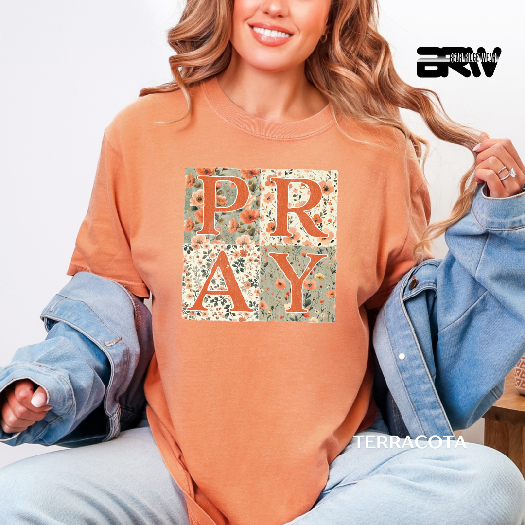 Person wearing a terracotta-colored sweatshirt with 'PRAY' print, sitting on a white background.
