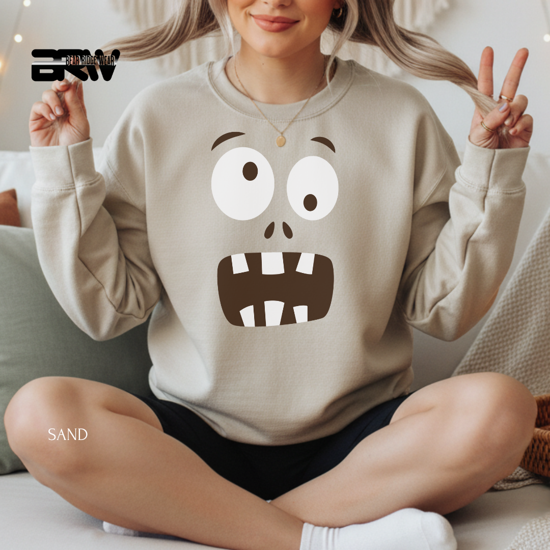 Person wearing a beige sweatshirt with a cartoon face design, sitting on a couch.