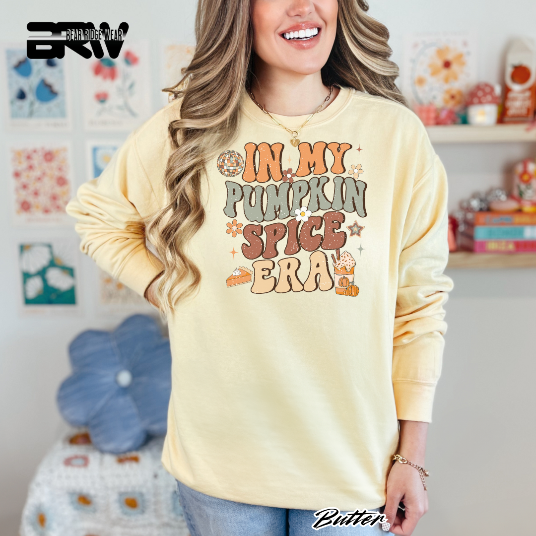 Woman wearing a yellow sweatshirt with 'In My Pumpkin Spice Era' text in a casual setting.