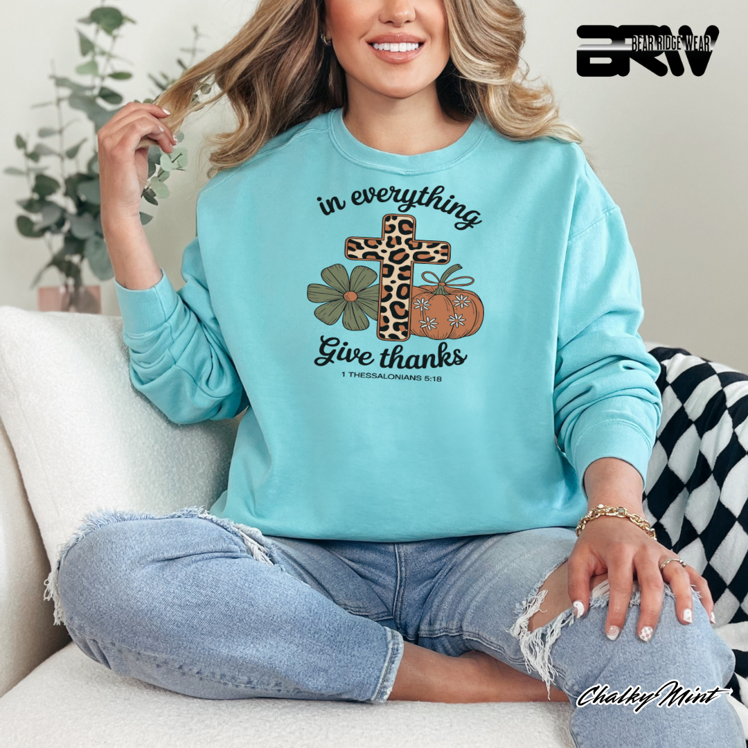 Woman wearing a light blue sweatshirt with a cross and flowers design, sitting on a couch.