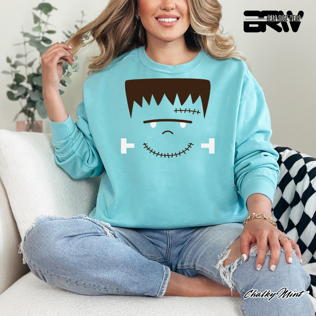 Person wearing a light blue sweatshirt with a cartoon face design, sitting on a couch.