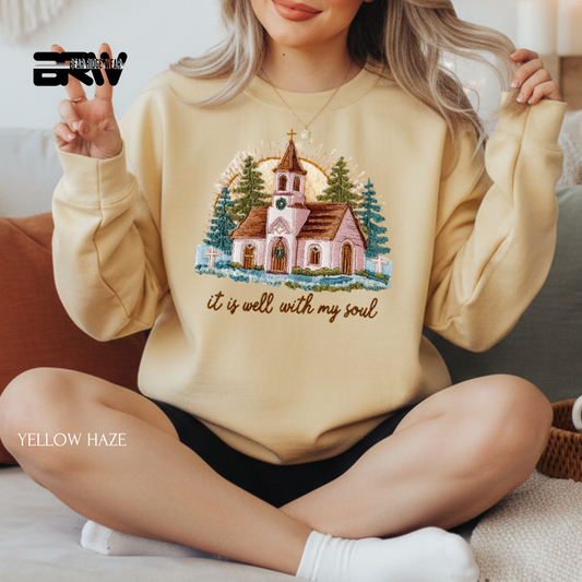 Person wearing a yellow sweatshirt with a church design and text, sitting on a couch.