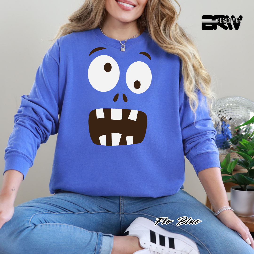 Person wearing a blue sweatshirt with a cartoon face design, sitting indoors.
