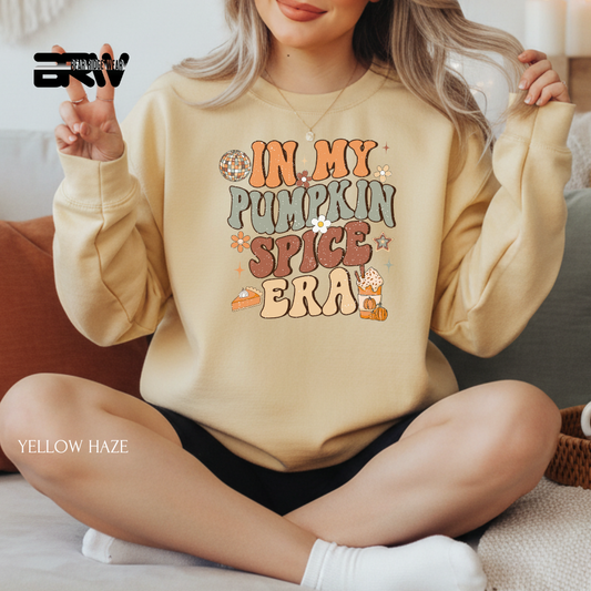 Person wearing a beige sweatshirt with 'In My Pumpkin Spice Era' text, sitting on a couch.