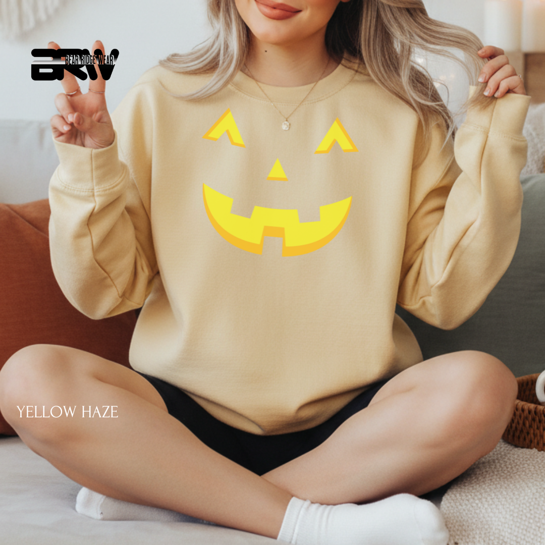 Person wearing a beige sweatshirt with a yellow jack-o'-lantern face design, sitting on a couch.