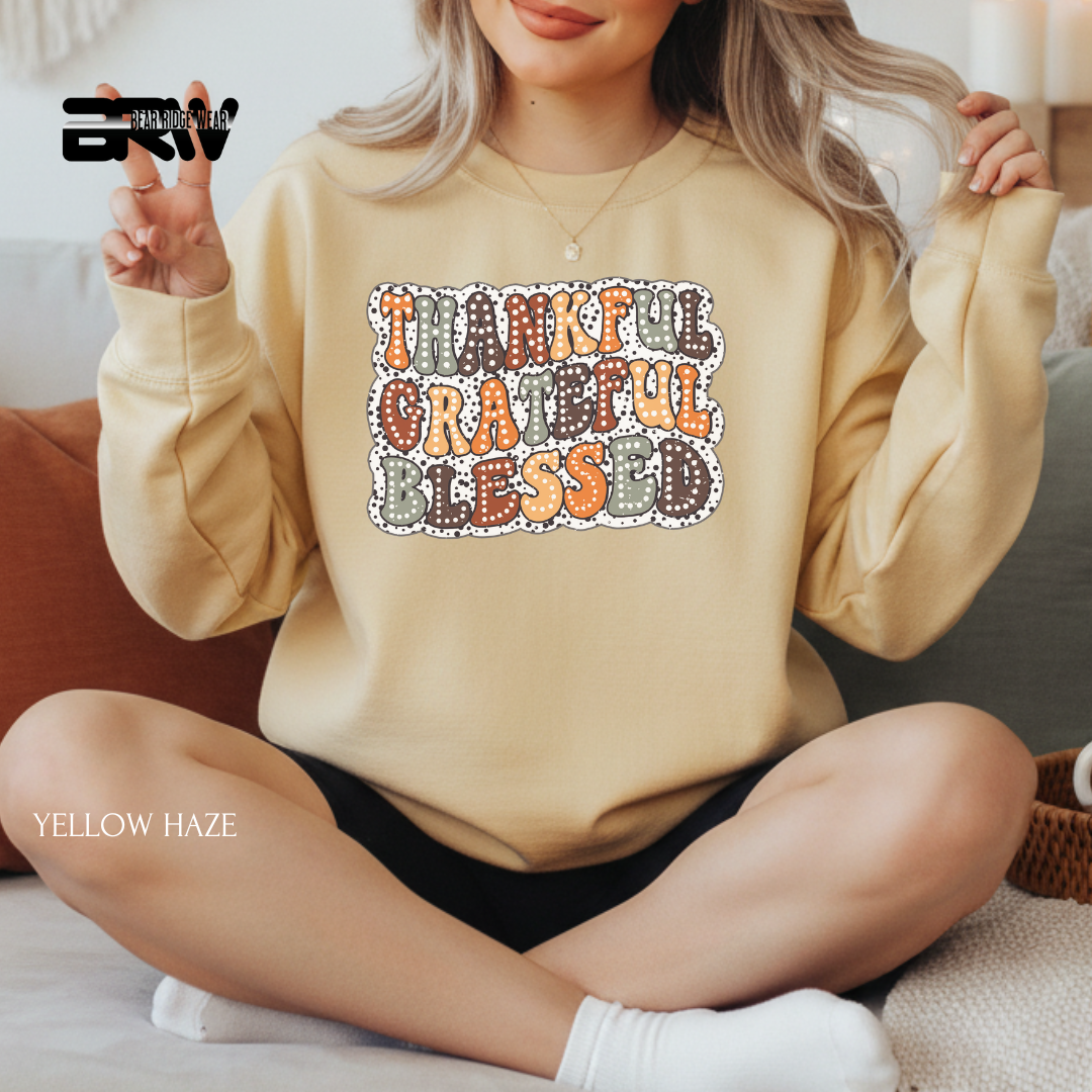 Person wearing a beige sweatshirt with 'Thankful Grateful Blessed' text, sitting on a couch.