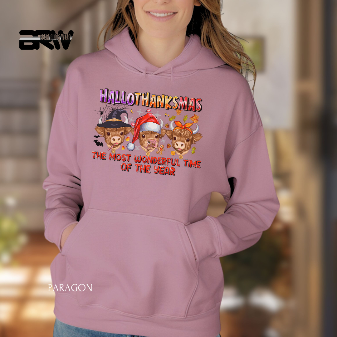Person wearing a pink hoodie with 'HALLOTHANKSMAS' design, featuring cartoon cows in festive hats.
