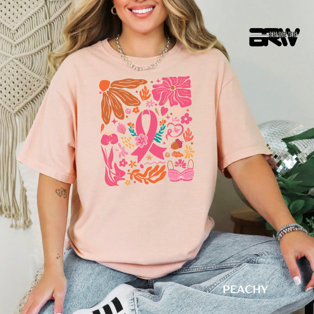 Person wearing a peach-colored t-shirt with a colorful design, sitting against a neutral background. BREAST CANCER AWARENESS SHIRT 