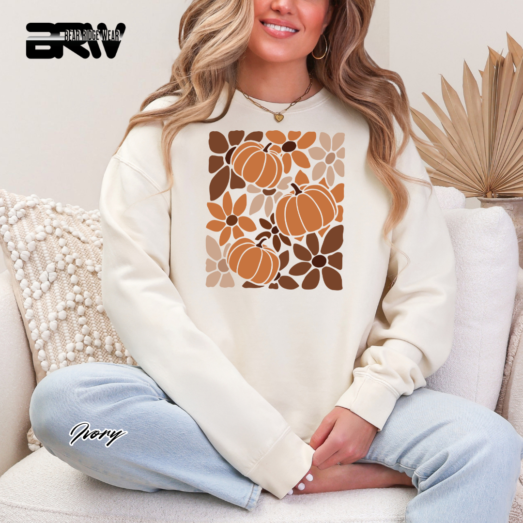 Woman wearing a cream sweatshirt with pumpkin design sitting on a couch.