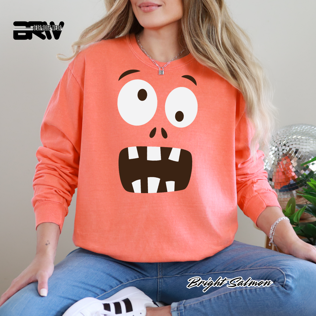Person wearing a bright salmon-colored sweatshirt with a cartoon face design, sitting on a chair.