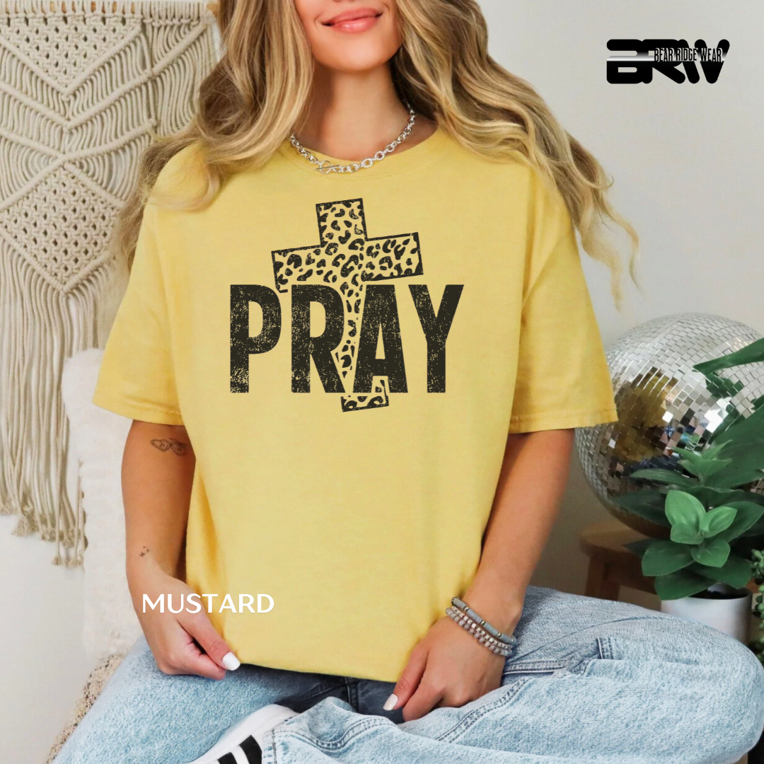 Person wearing a yellow t-shirt with 'PRAY' and a cross design, sitting in a casual setting.
