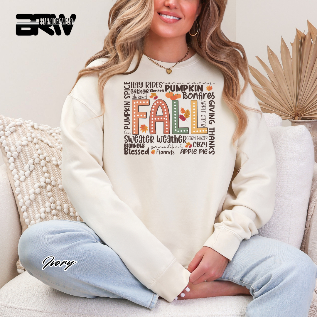 Woman wearing a cream sweatshirt with 'Fall' and autumn-themed text, sitting on a couch.