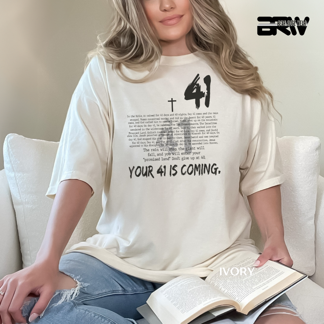 Person wearing a white t-shirt with text, sitting on a couch with an open book.