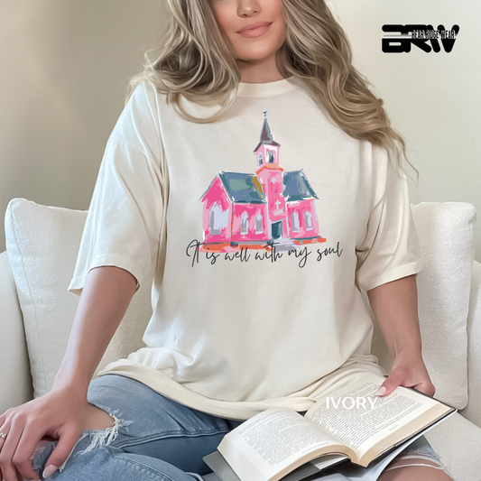 Person wearing a t-shirt with a church design and text, sitting on a couch with an open book.