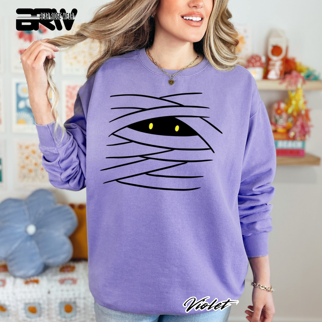 Person wearing a purple sweatshirt with a black eye design, standing in a room with colorful decor.