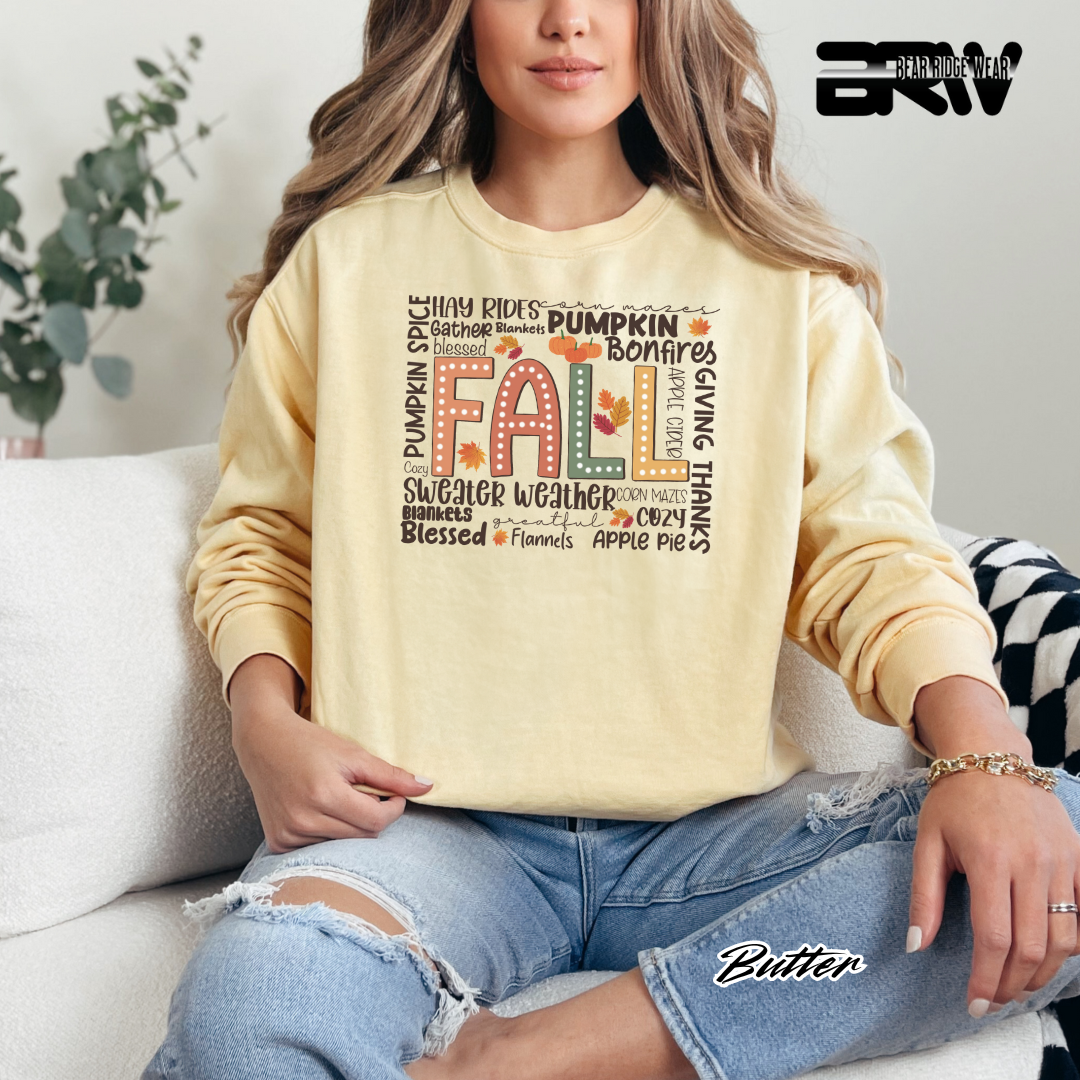 Person wearing a yellow sweatshirt with 'Fall' text and autumnal graphics, sitting on a couch.