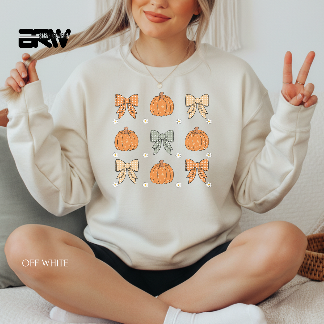 Person wearing an off-white sweatshirt with pumpkins and bows design, sitting on a couch.