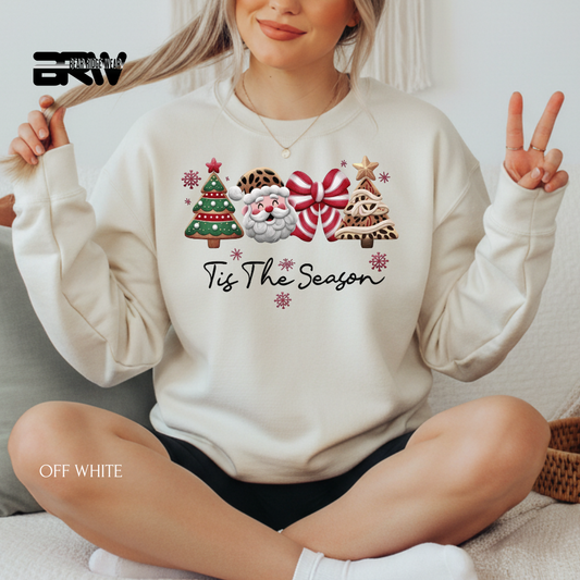Person wearing a white sweatshirt with Christmas-themed designs and text, sitting on a couch.